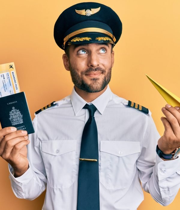Handsome hispanic pilot man holding paper plane and passport smiling looking to the side and staring away thinking.
